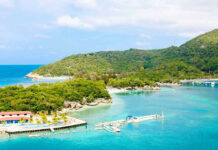 Tropical beach with docks and lush green hills.
