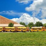 Terrifying School Bus Ordeal—Kids Trapped, Parents Rage A row of yellow school buses parked in front of a school building under a cloudy sky