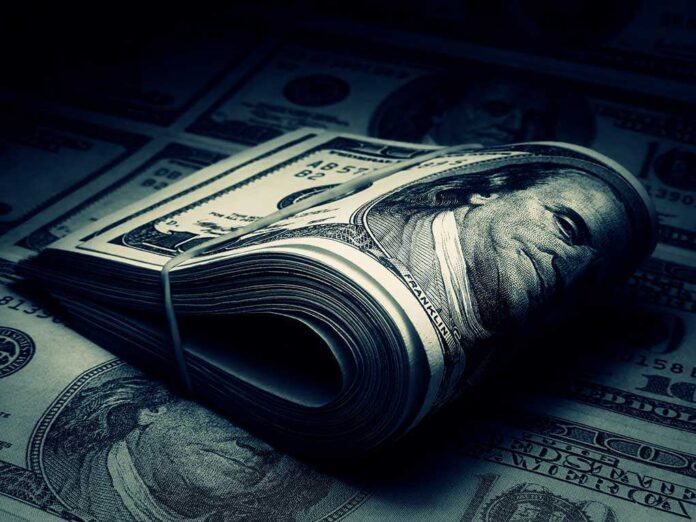 shutterstock_125542373.jpg A rolled stack of hundred dollar bills on a background of more banknotes