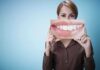 A woman holding a large image of a smiling mouth in front of her face