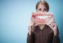 HORRIFYING Discovery Links Brushing to Deadly Cancer A woman holding a large image of a smiling mouth in front of her face