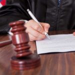 A judge signing a legal document with a gavel in the foreground