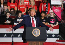 Trump’s Christmas SURPRISE: Latest Approval Soars! Politician speaking at rally with supporters behind him.