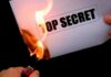 A hand holding a lighter igniting a paper labeled TOP SECRET as it catches fire