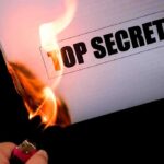 A hand holding a lighter igniting a paper labeled TOP SECRET as it catches fire