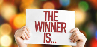 Hands holding a sign reading The Winner Is