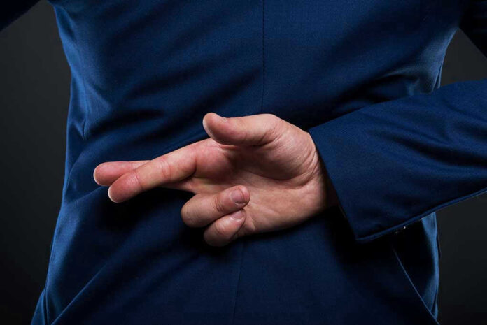 751558732 Crossed fingers behind back in blue suit.