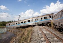 An overturned train on a railway track surrounded by vegetation