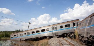 An overturned train on a railway track surrounded by vegetation