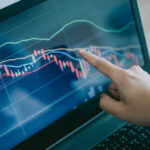 IRON FIST Slashes Murder Rate by 98% Hand pointing at stock market graph on laptop screen.