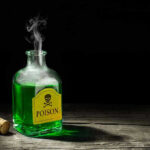 Green poison bottle with cork on wooden surface.