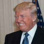 Liberal Media MELTDOWN After Trump SOTU A smiling man in formal attire with an American flag in the background