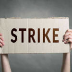 UNPRECEDENTED Strike Could CHOKE Nationwide FOOD Distribution Two hands holding a cardboard sign saying STRIKE.