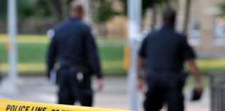 Police officers walking past caution tape at a crime scene