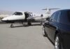 A private jet parked at an airport with a luxury car in the foreground