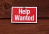 A red and white Help Wanted sign pinned to a wooden surface