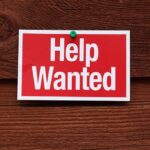 A red and white Help Wanted sign pinned to a wooden surface