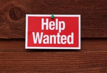 A red and white Help Wanted sign pinned to a wooden surface