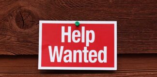 A red and white Help Wanted sign pinned to a wooden surface
