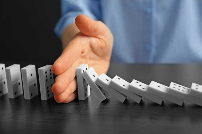 509251924 Hand stopping falling row of dominoes.