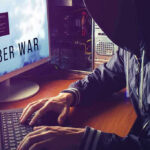 Hacker typing at desk with Cyber War screen.