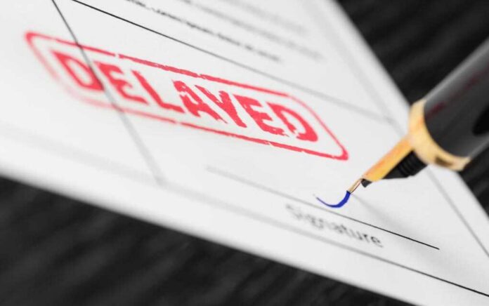 shutterstock_1022165809-3- A close-up of a document with a red 'DELAYED' stamp and a fountain pen poised to sign