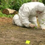Chilling Bear Encounter: Hiker’s Gruesome End Forensic investigator in a protective suit collecting evidence from the ground