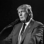 A public figure speaking into a microphone in a serious manner