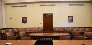 Empty courtroom with wooden tables, chairs, and a door.