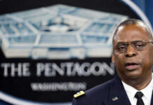 Trump’s War-Footing Stuns Wall Street Man speaking in front of Pentagon sign.