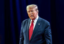 Chicago Bloodshed Ignites Trump Showdown Man in suit with red tie speaking on stage.