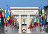 Iran Seeks UN Seal of Approval Nuclear Agreement United Nations building with numerous national flags outside.