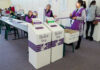 California Vote Delays Fuel Election Suspicion Debate Election polling station with ballot boxes and officials.