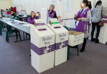California Vote Delays Fuel Election Suspicion Debate Election polling station with ballot boxes and officials.