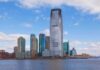 A modern city skyline featuring tall buildings along a waterfront under a cloudy sky