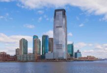 A modern city skyline featuring tall buildings along a waterfront under a cloudy sky