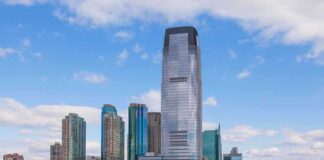 A modern city skyline featuring tall buildings along a waterfront under a cloudy sky