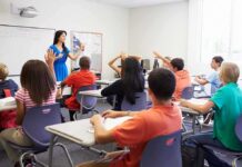 Teacher Fired After Student Kiss Skit Controversy Teacher in a blue dress instructing students in a classroom with hands raised