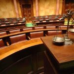 Death Penalty Considered in Guard Ambush Case A courtroom with empty seats and a scale of justice in the foreground