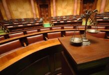 Death Penalty Considered in Guard Ambush Case A courtroom with empty seats and a scale of justice in the foreground