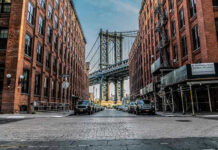 NYC Freezes Rents — Now What Breaks? Street view with bridge between two brick buildings.