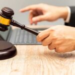 Judge's gavel held over block near laptop on wooden desk
