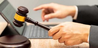 Judge's gavel held over block near laptop on wooden desk