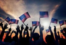 Haaland’s Goodbye Shocks America Silhouetted crowd holding American flags against a sunset sky