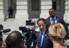 Man in suit speaks to reporters outside a government building