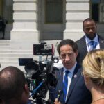 Man in suit speaks to reporters outside a government building