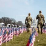 Two soldiers walk among American flags toward the U.S. Capitol