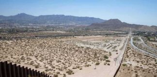 Border fence cutting across a desert landscape with mountains in the distance