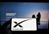 Smartphone showing Starlink logo in front of a computer screen