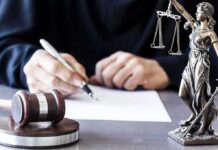 Judge writing at desk with gavel and Lady Justice statue